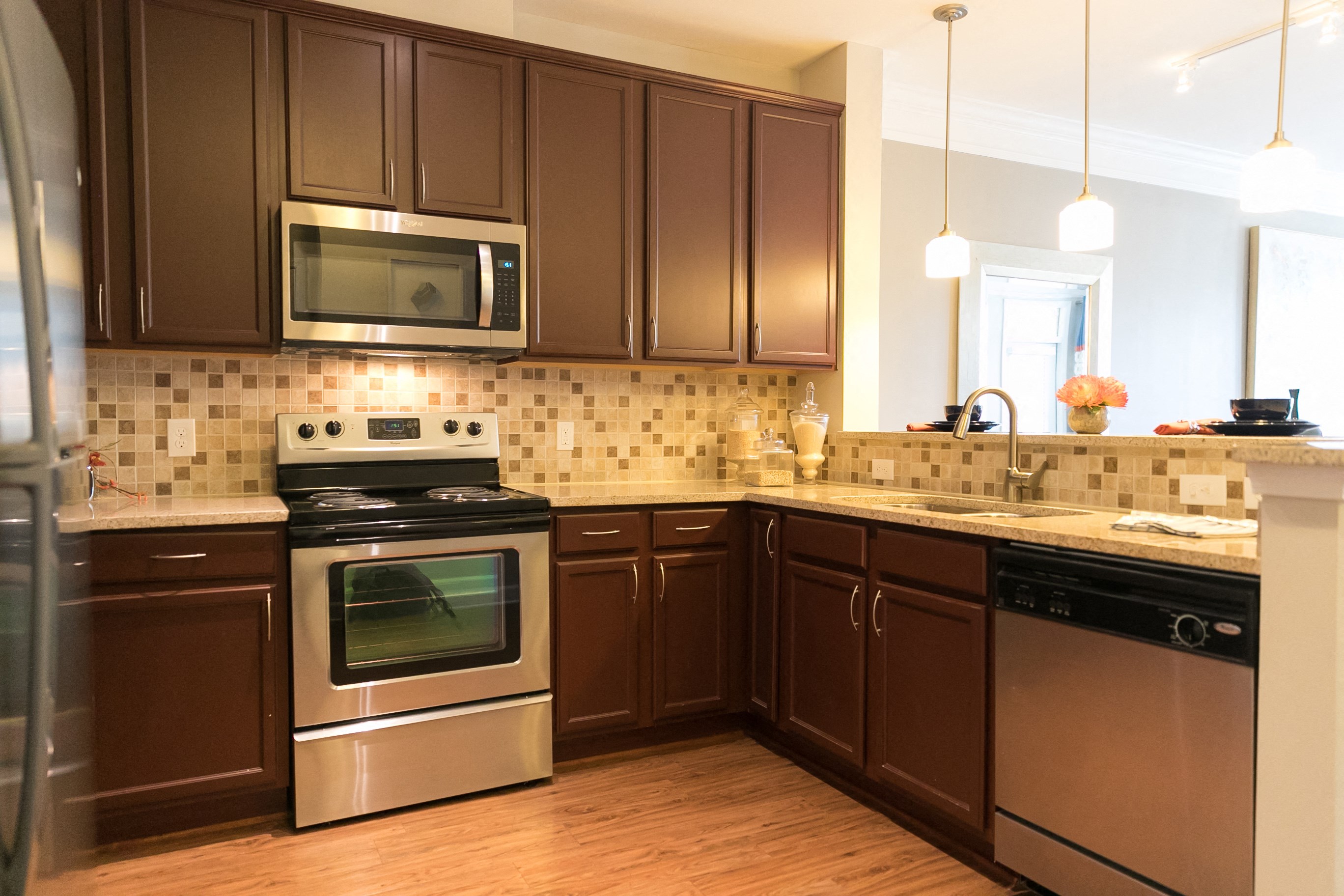 Kitchen area with brown cabinets, stainless steel appliances, tile backsplash, and granite countertops.